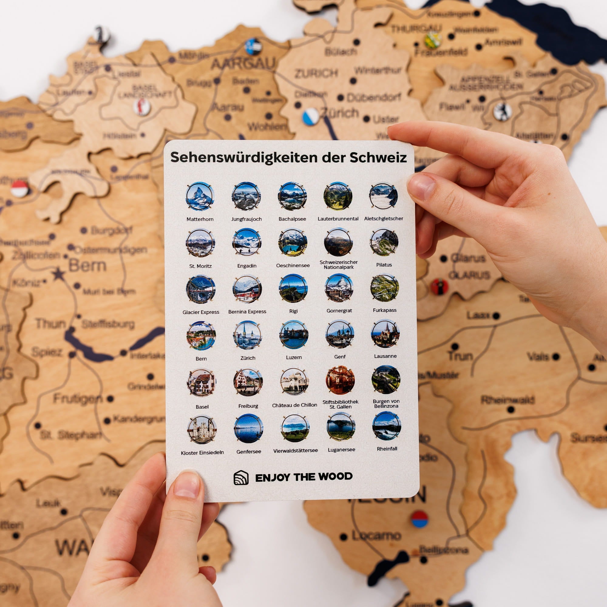 Wooden map of Switzerland with a card displaying icons of Swiss attractions held by hands.