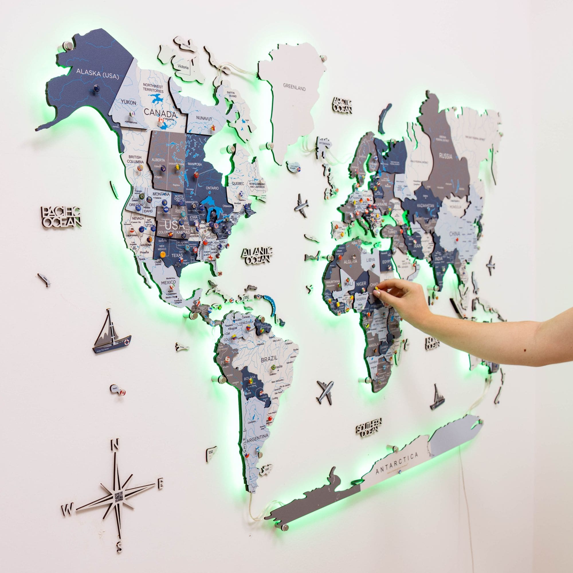 World map with LED lighting on a white wall, showing a hand interacting with it.
