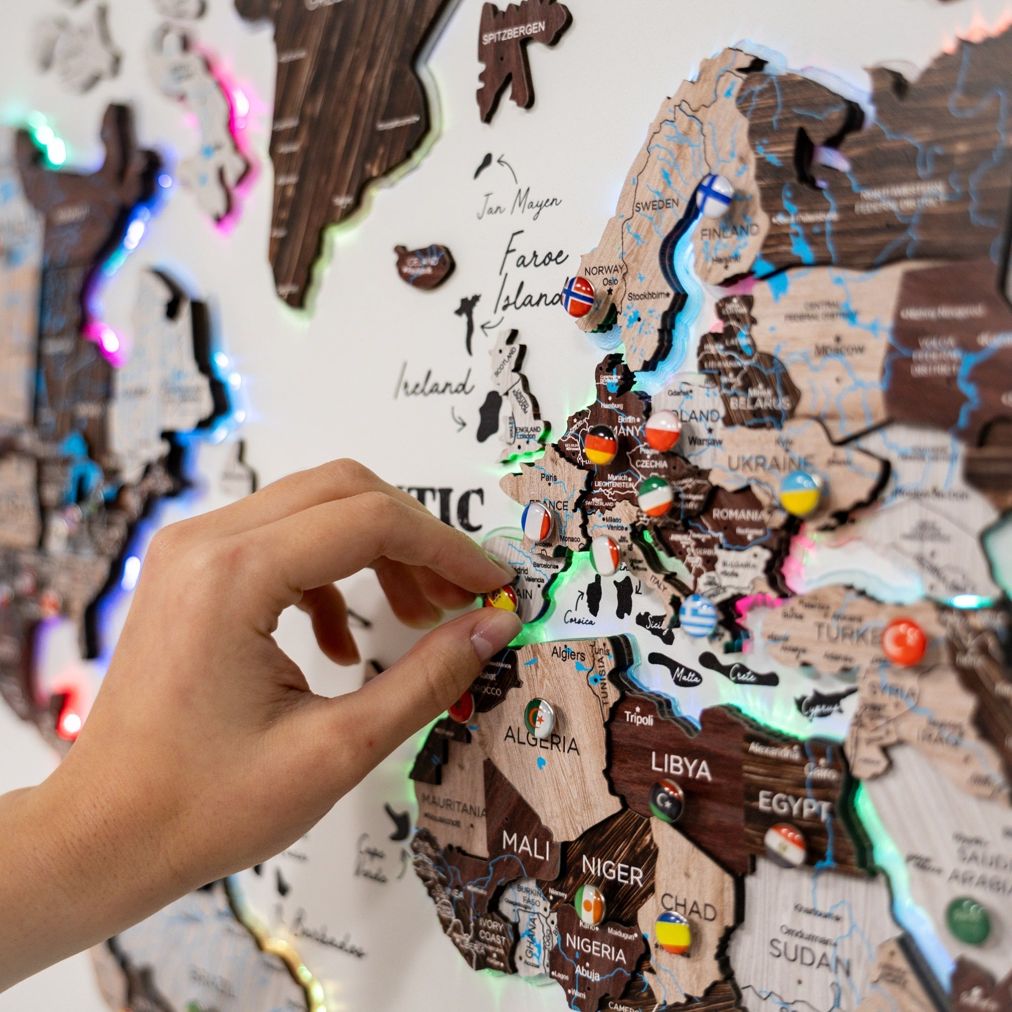 Hand placing a country flag pin on a wooden map of Africa with colorful pins.
