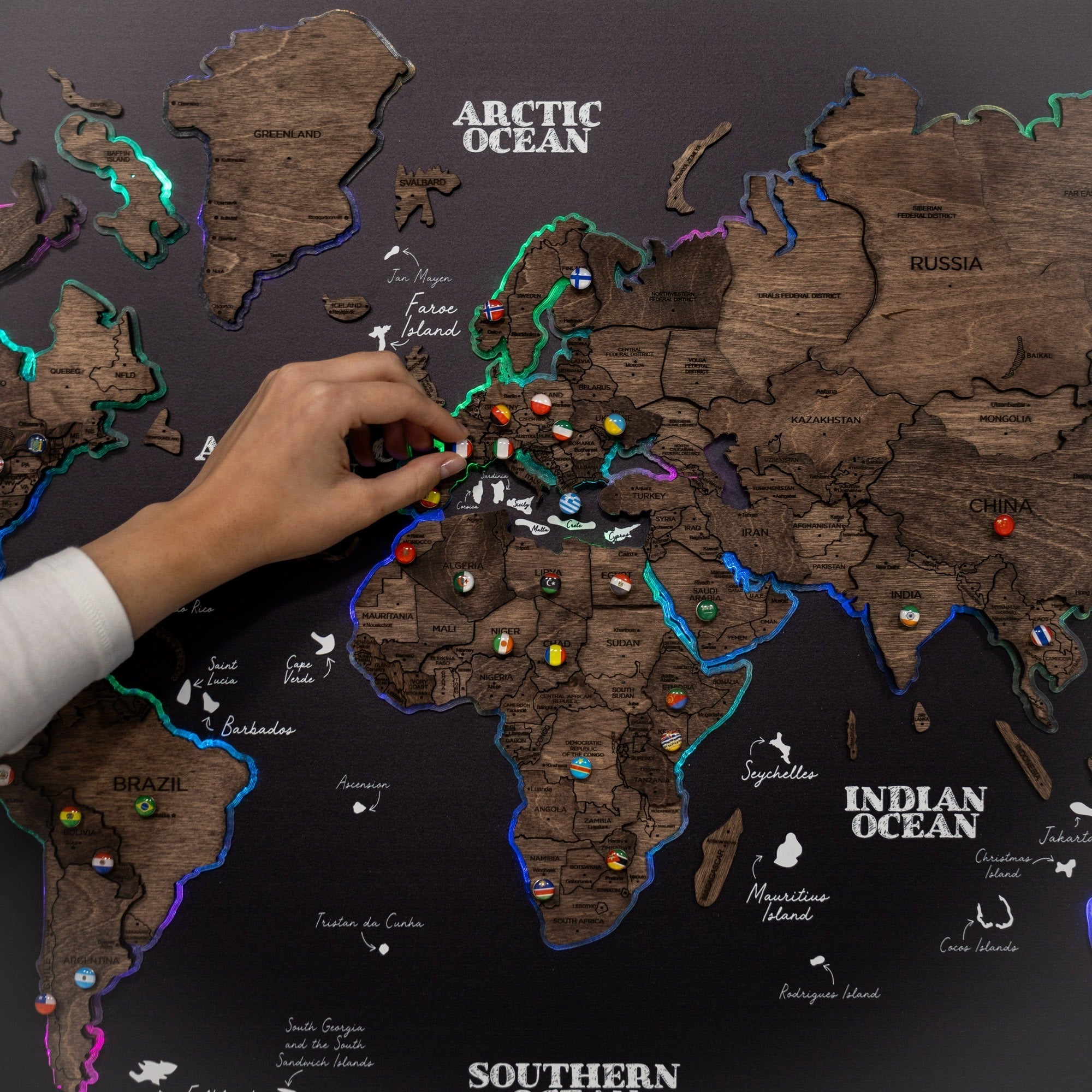 World map with wooden texture, hand pointing at a location, and colorful pins.