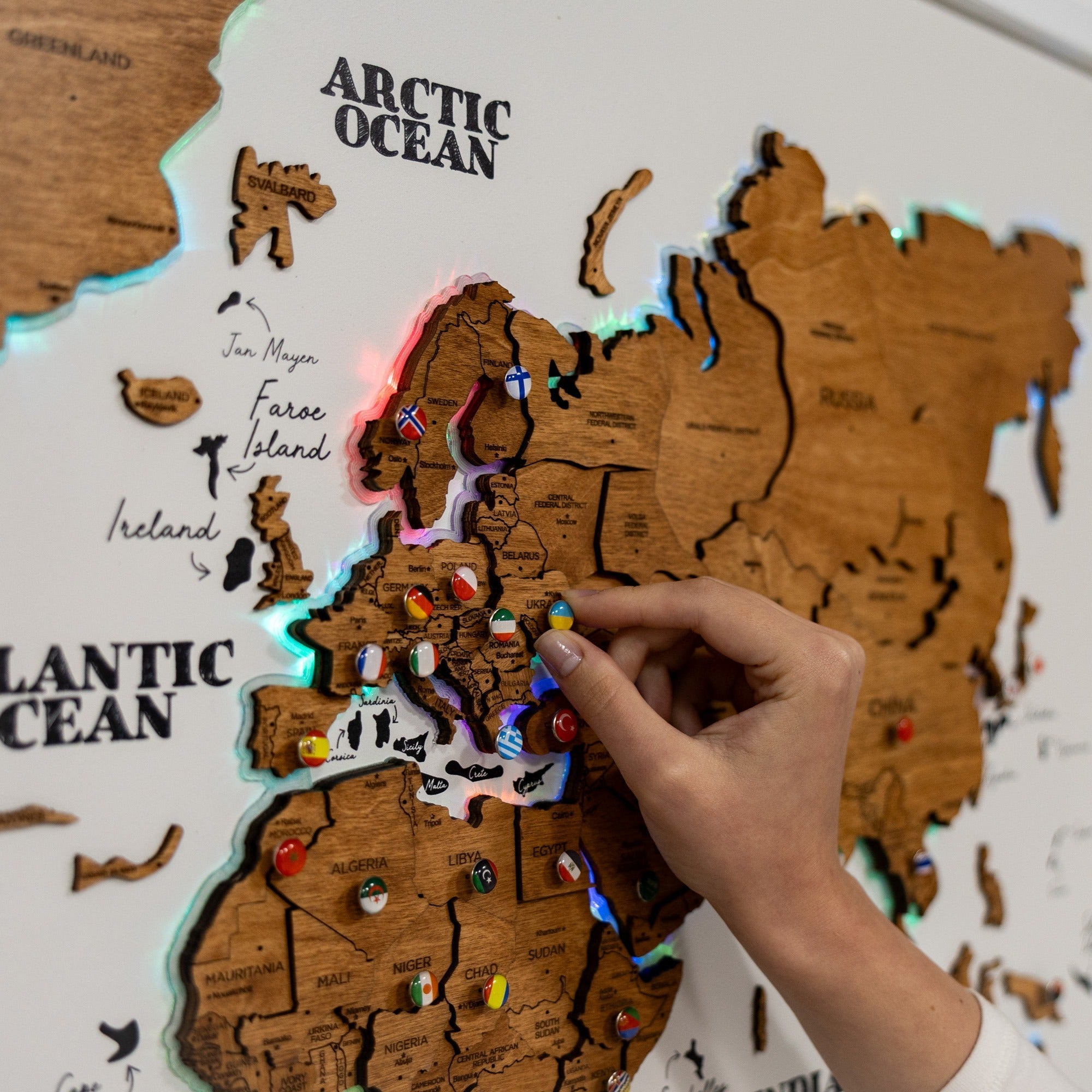 Wooden map of Europe with pinned locations, hand interacting with it.