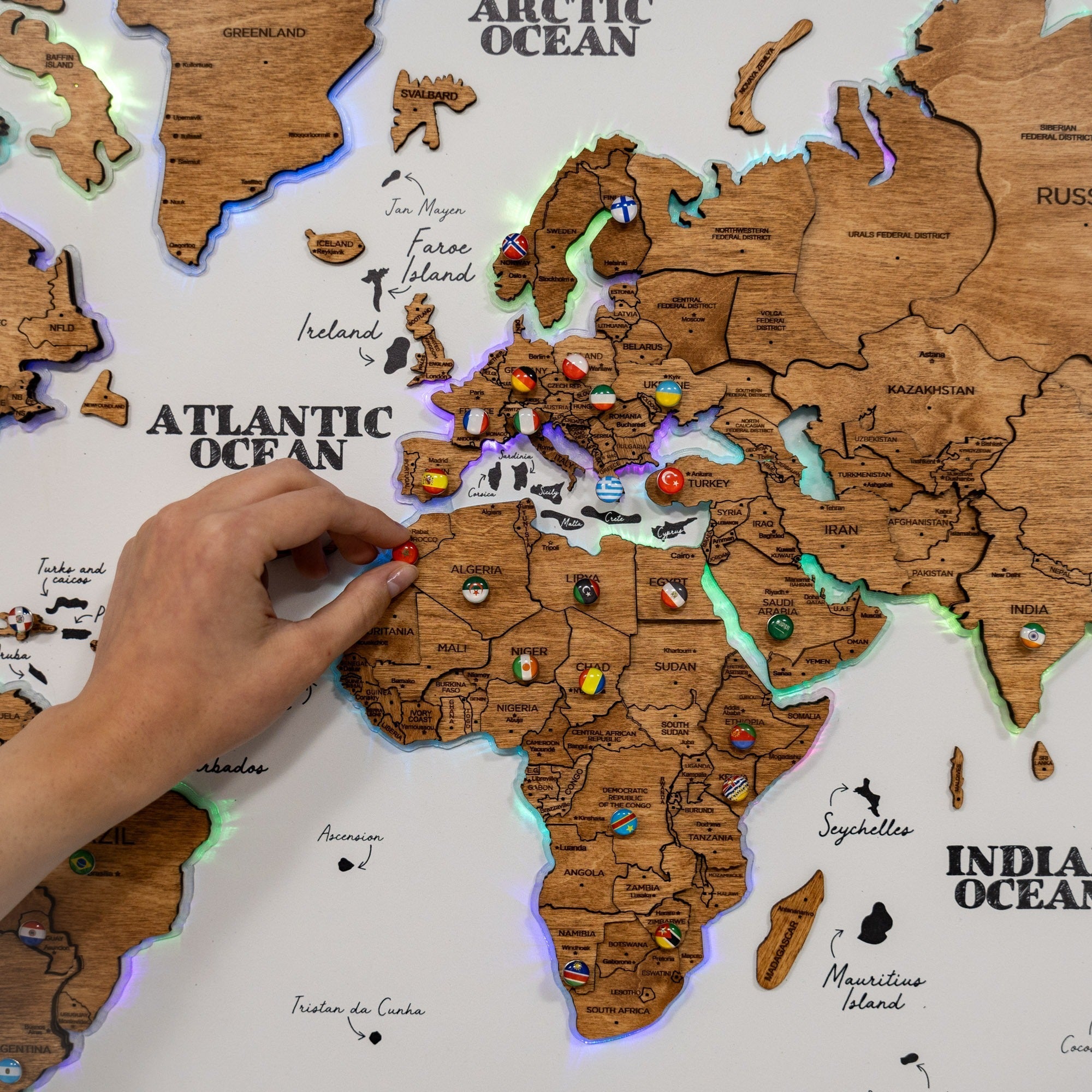 Wooden world map with colorful pins, hand interacting with it on a white background