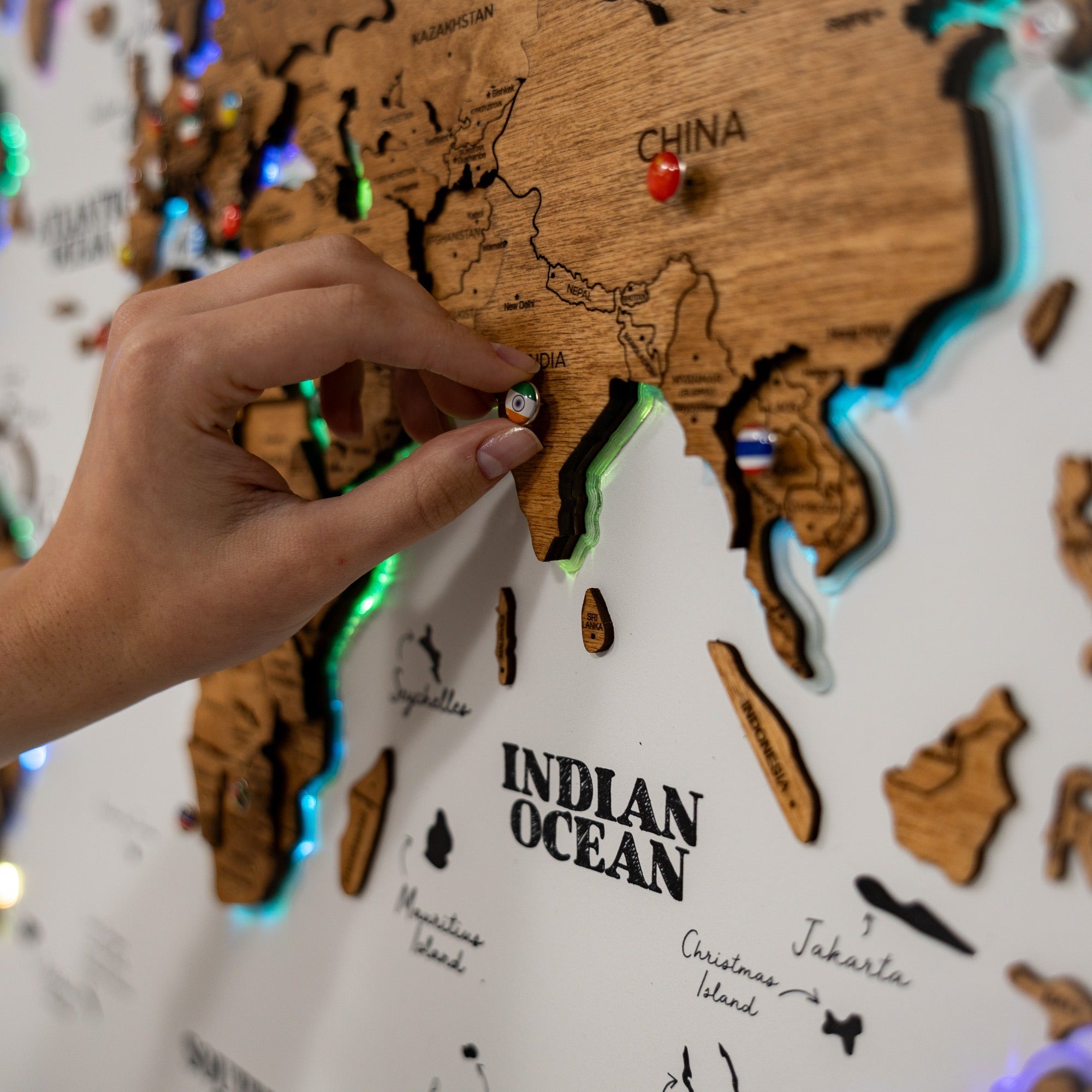 Hand placing a pin on a wooden map of the world, focusing on the Indian Ocean.