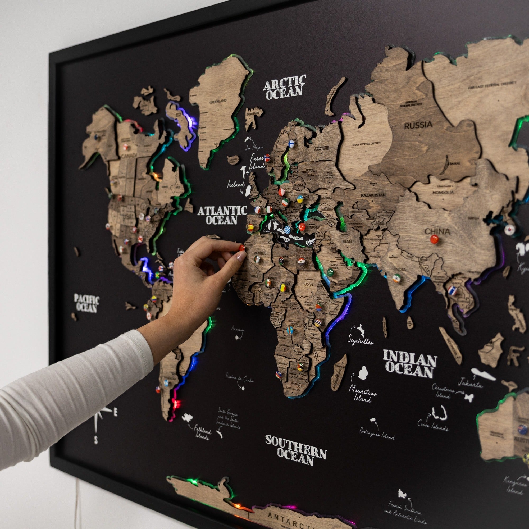 World map with pins on a black background, person pointing at a location.
