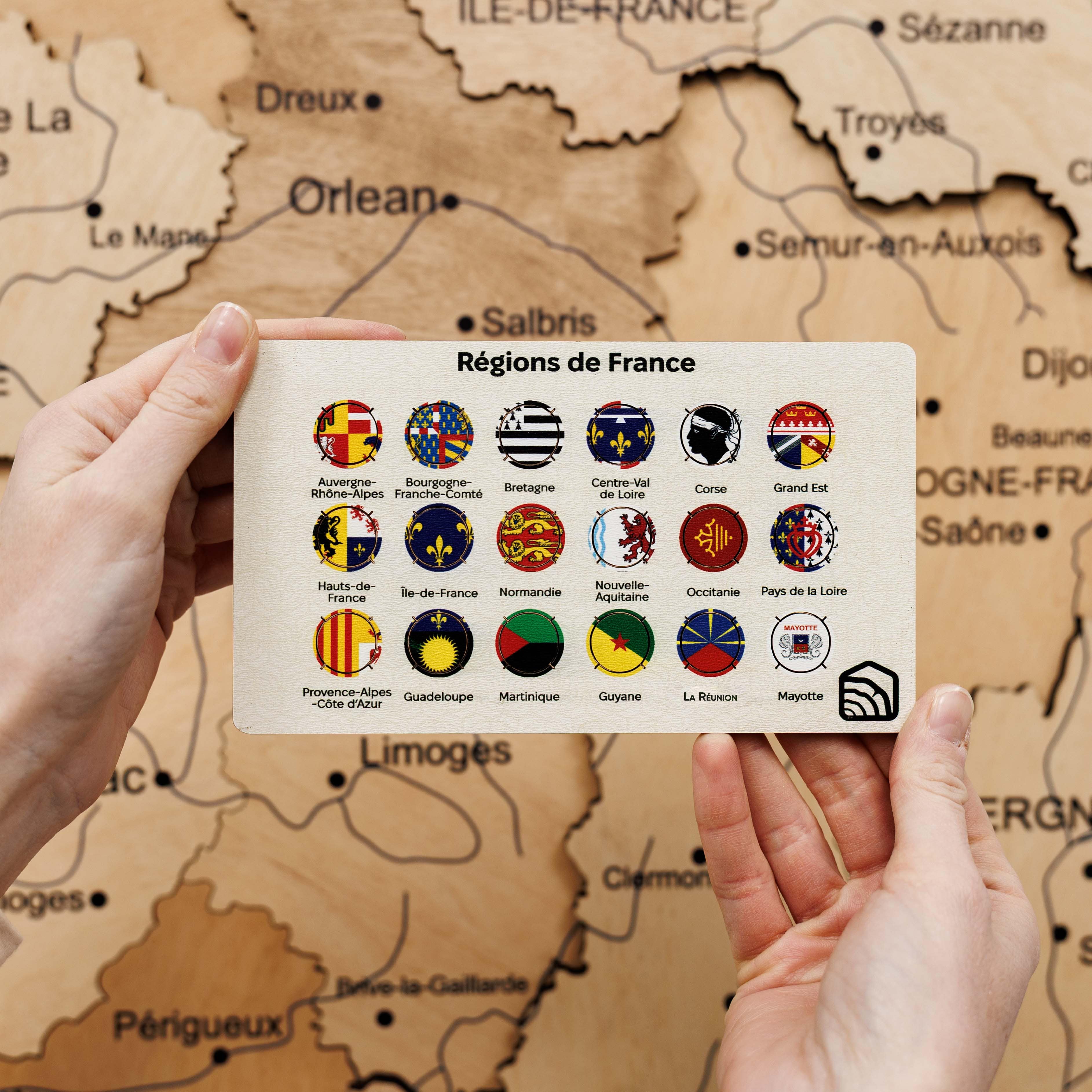 Map of France with regions displayed on a card held by hands against a map background.