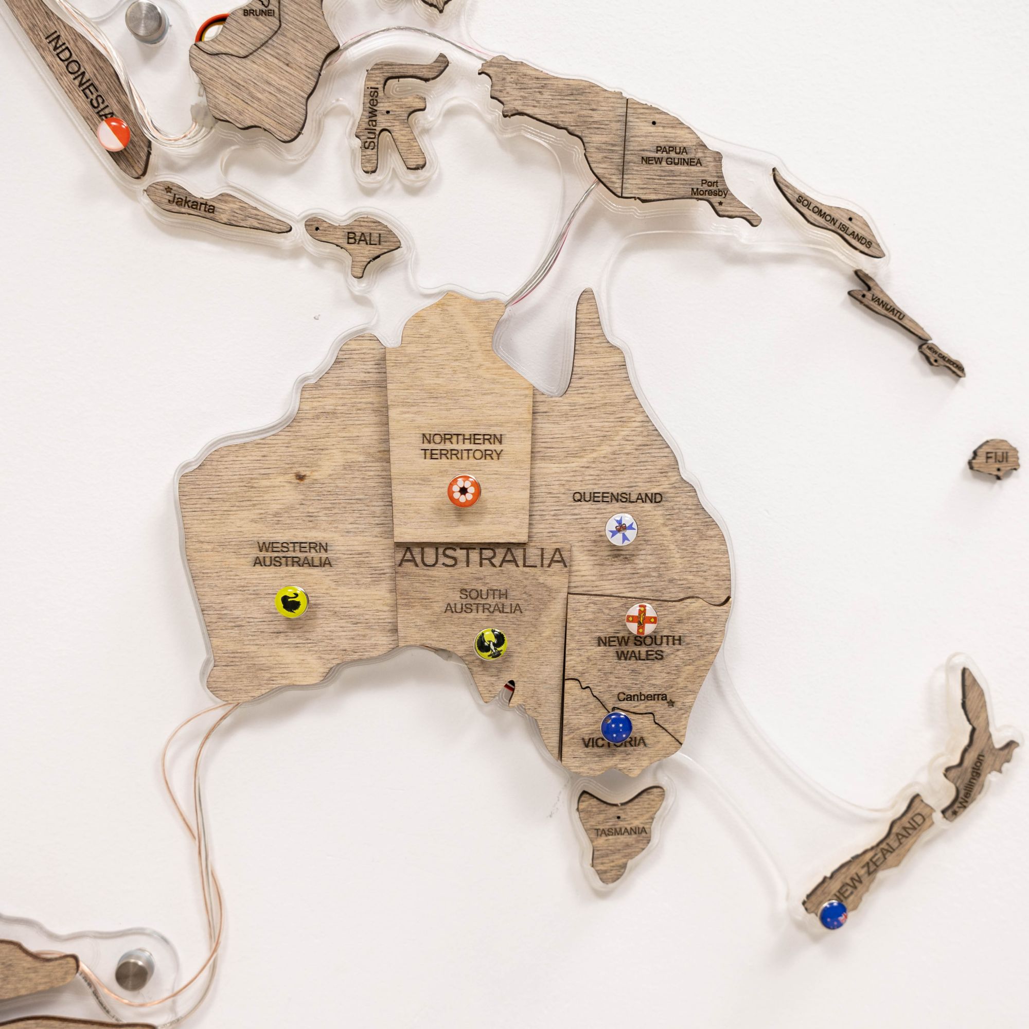 Wooden map of Australia with labeled states and pins on a white background