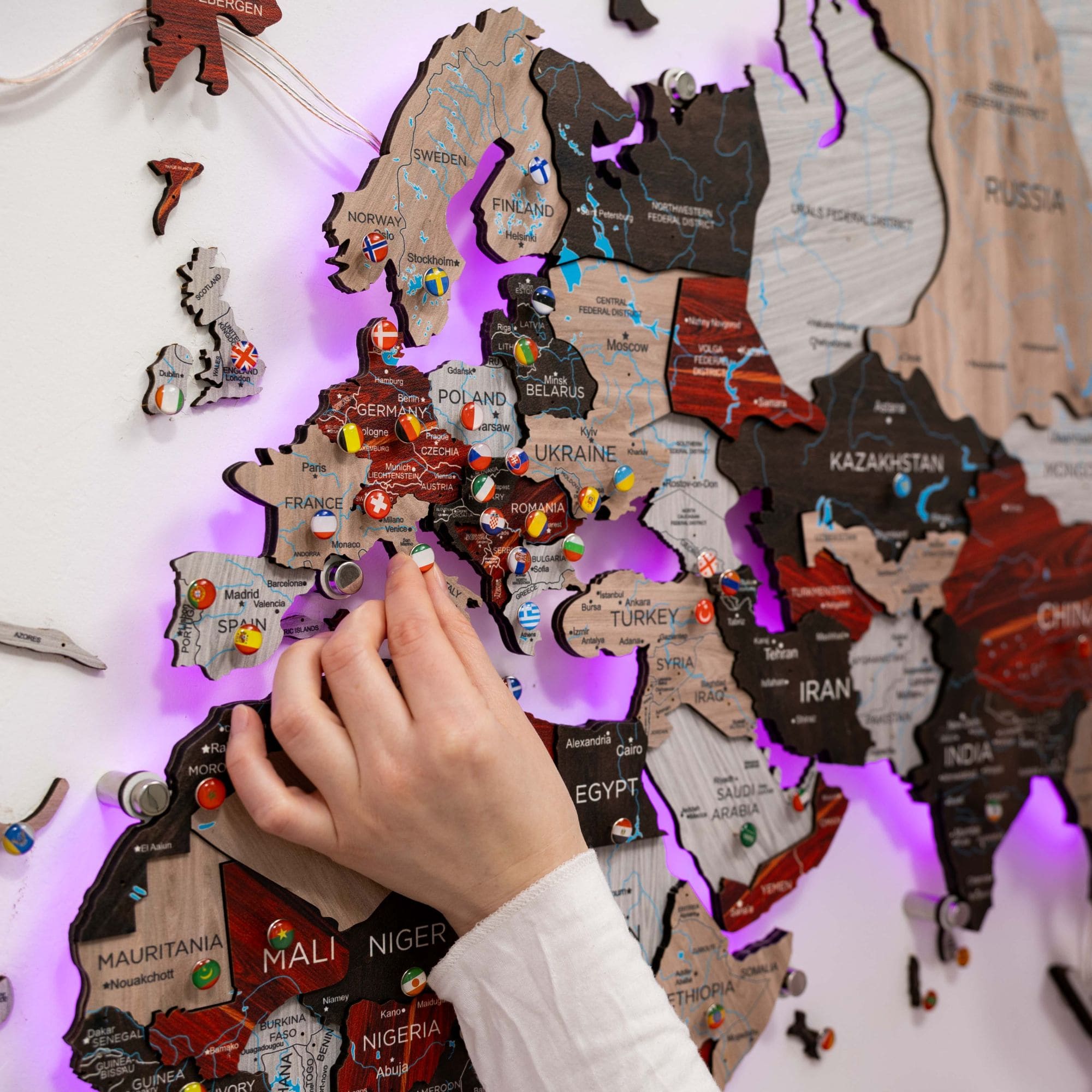 Hand placing a wooden puzzle piece on a world map with LED lighting.