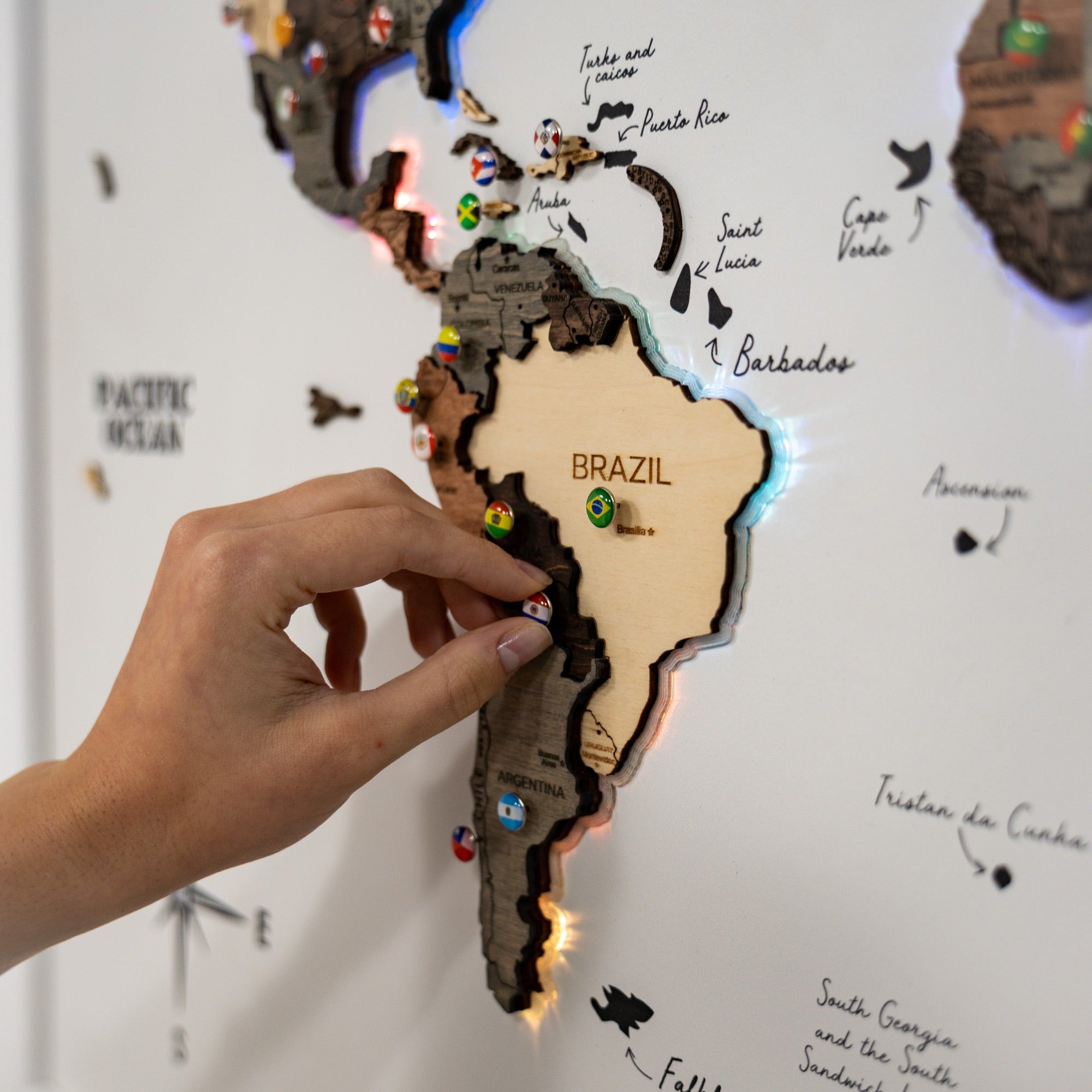 Hand interacting with a wooden map of South America, highlighting Brazil.
