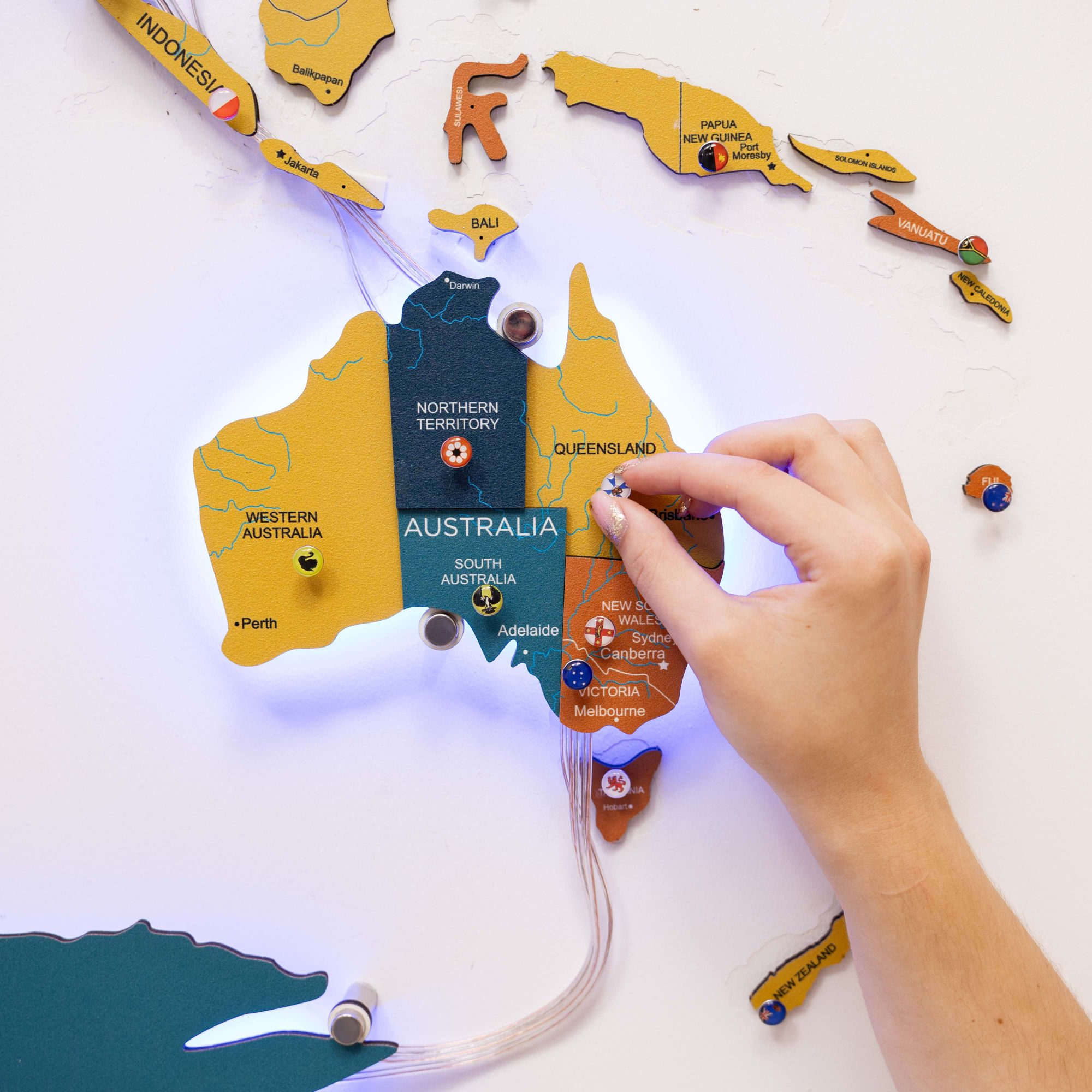 Hand interacting with a map of Australia made from wooden pieces on a white background