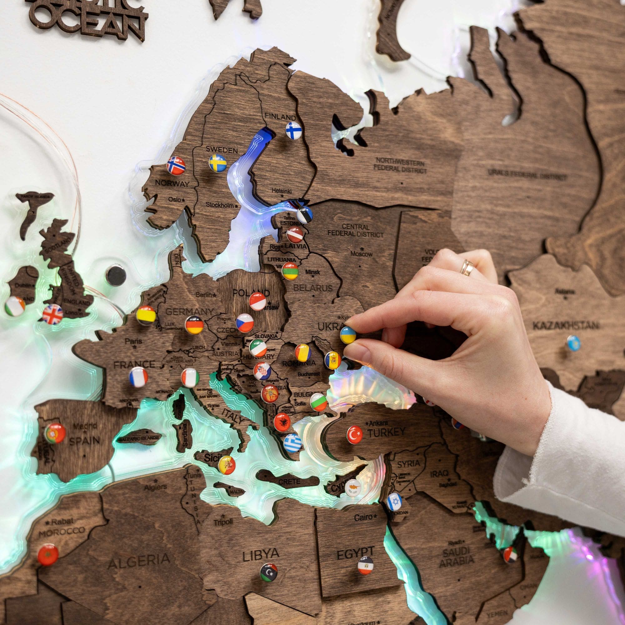 Wooden world map with pins marking locations, held by a hand.