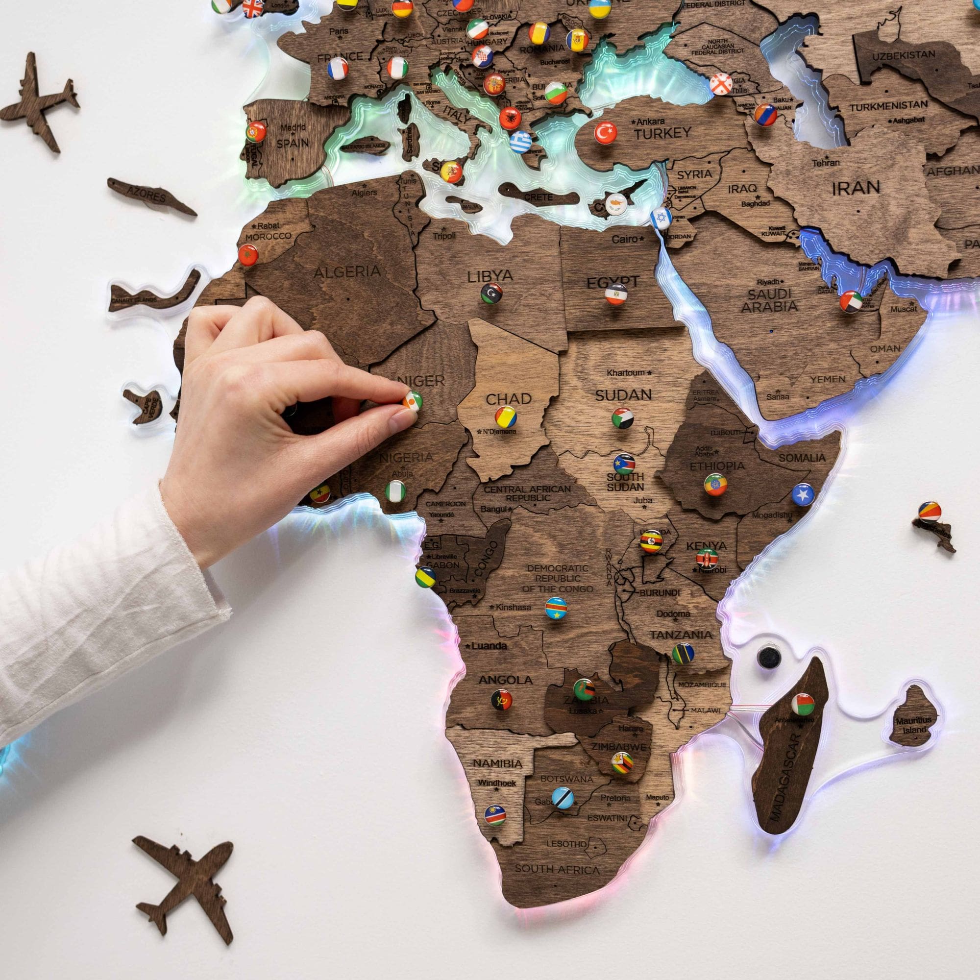 Wooden map of Africa with pins marking locations, held by a person.