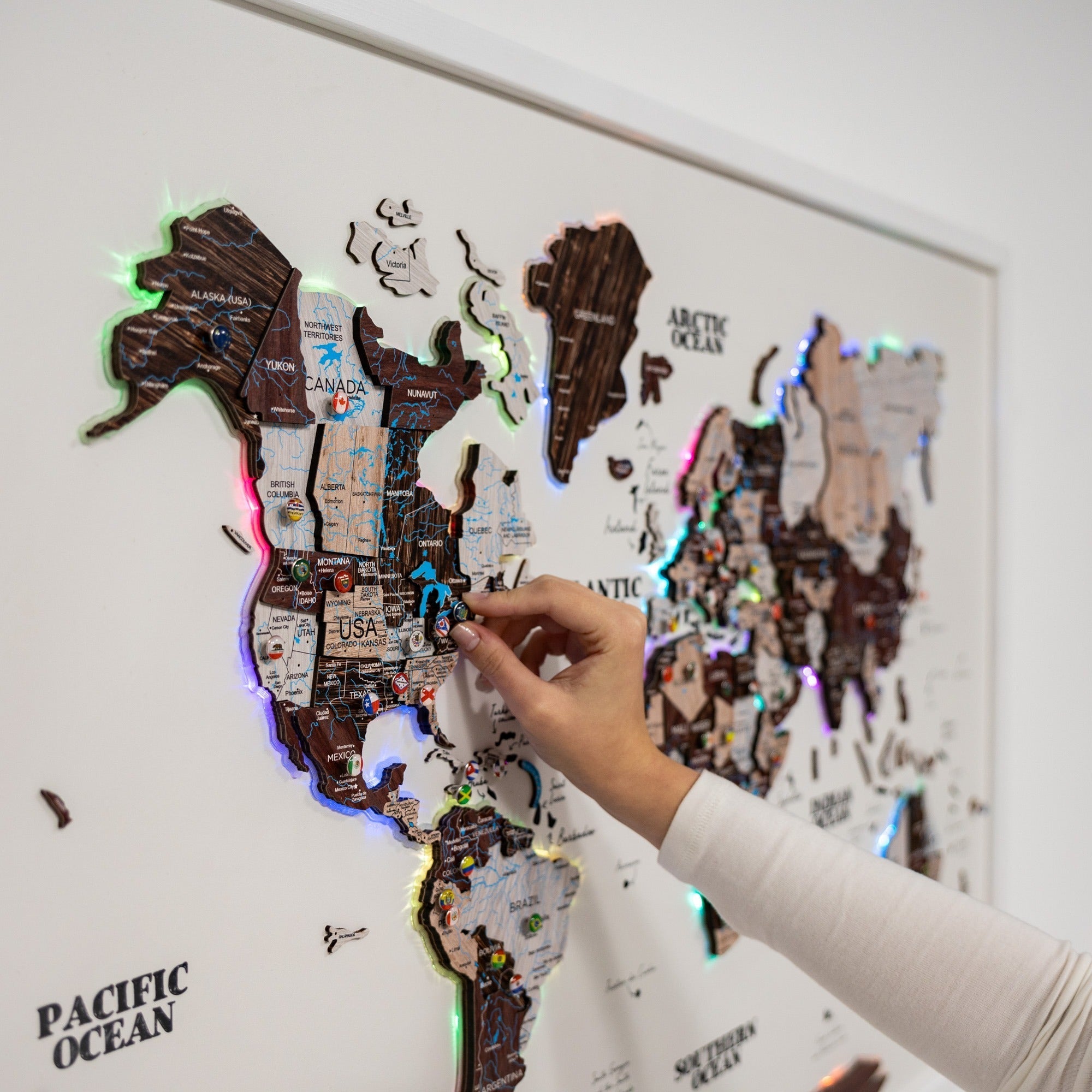 World map with LED lights on a white wall, hand pointing at a location.