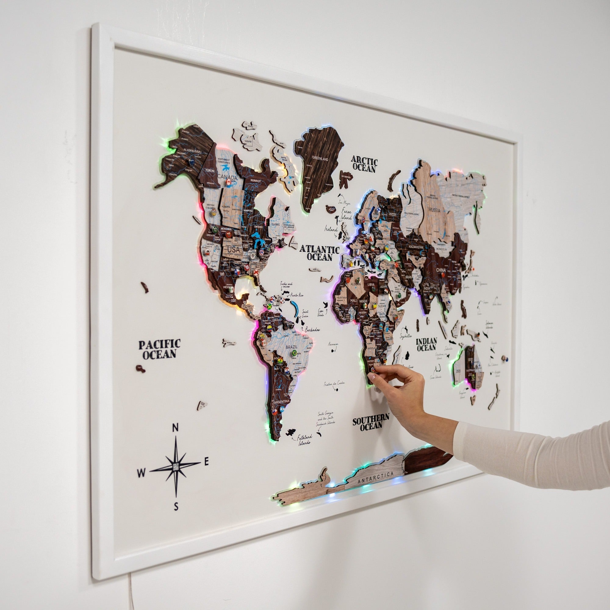 World map with LED lights on a white wall, showing a hand pointing at it.