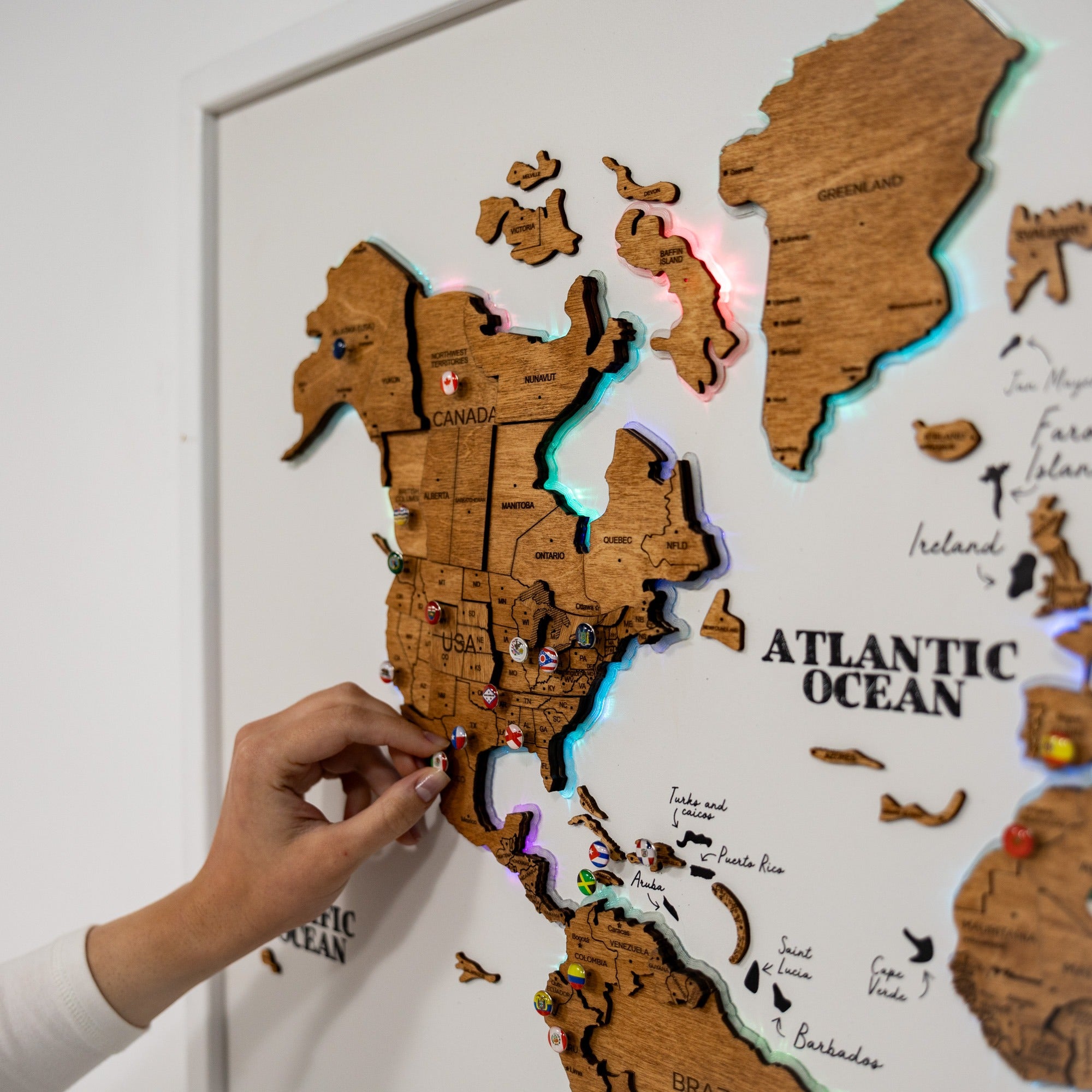 Wooden world map with pins on a white wall, hand placing a pin.