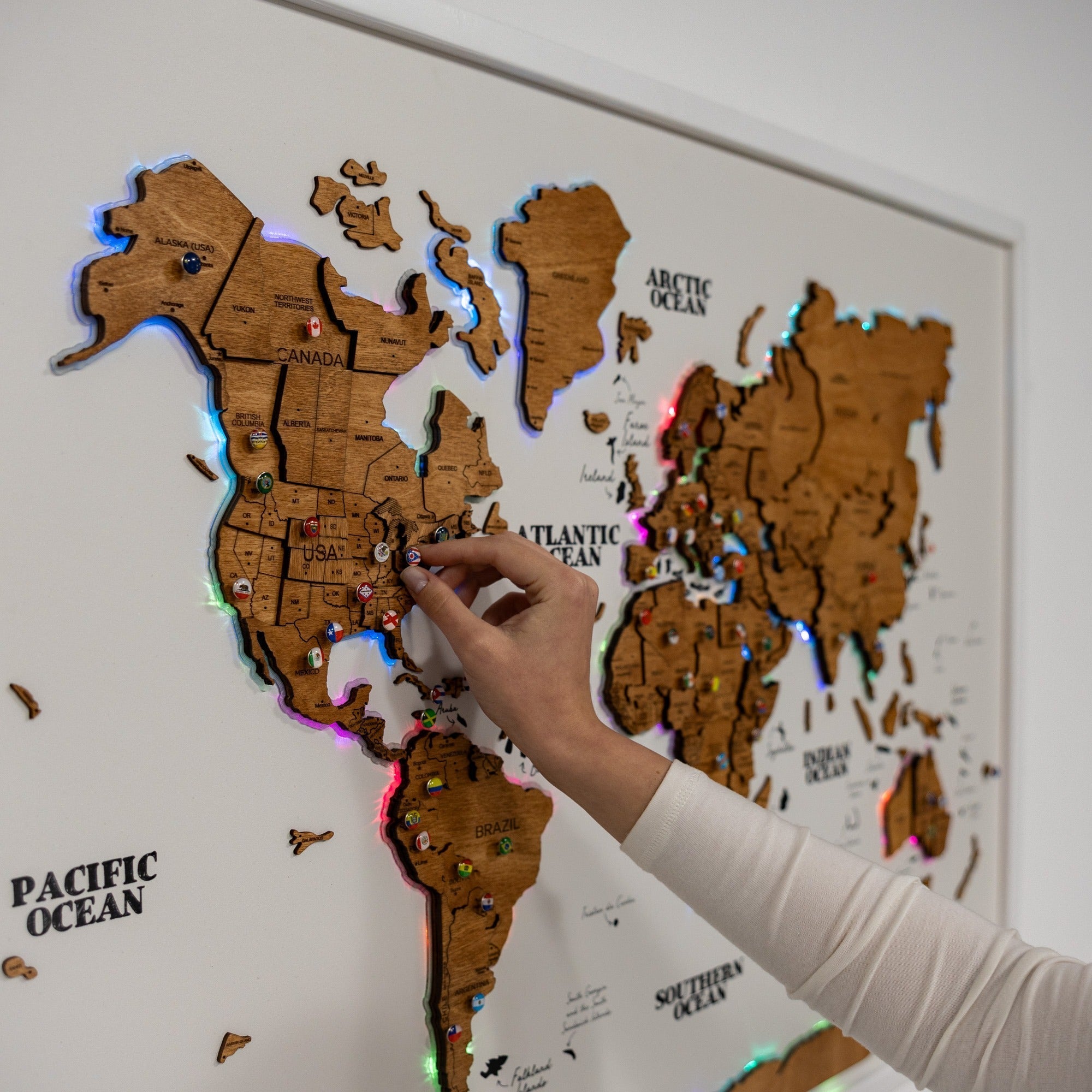 Wooden world map with LED lights and a hand pointing at a location.