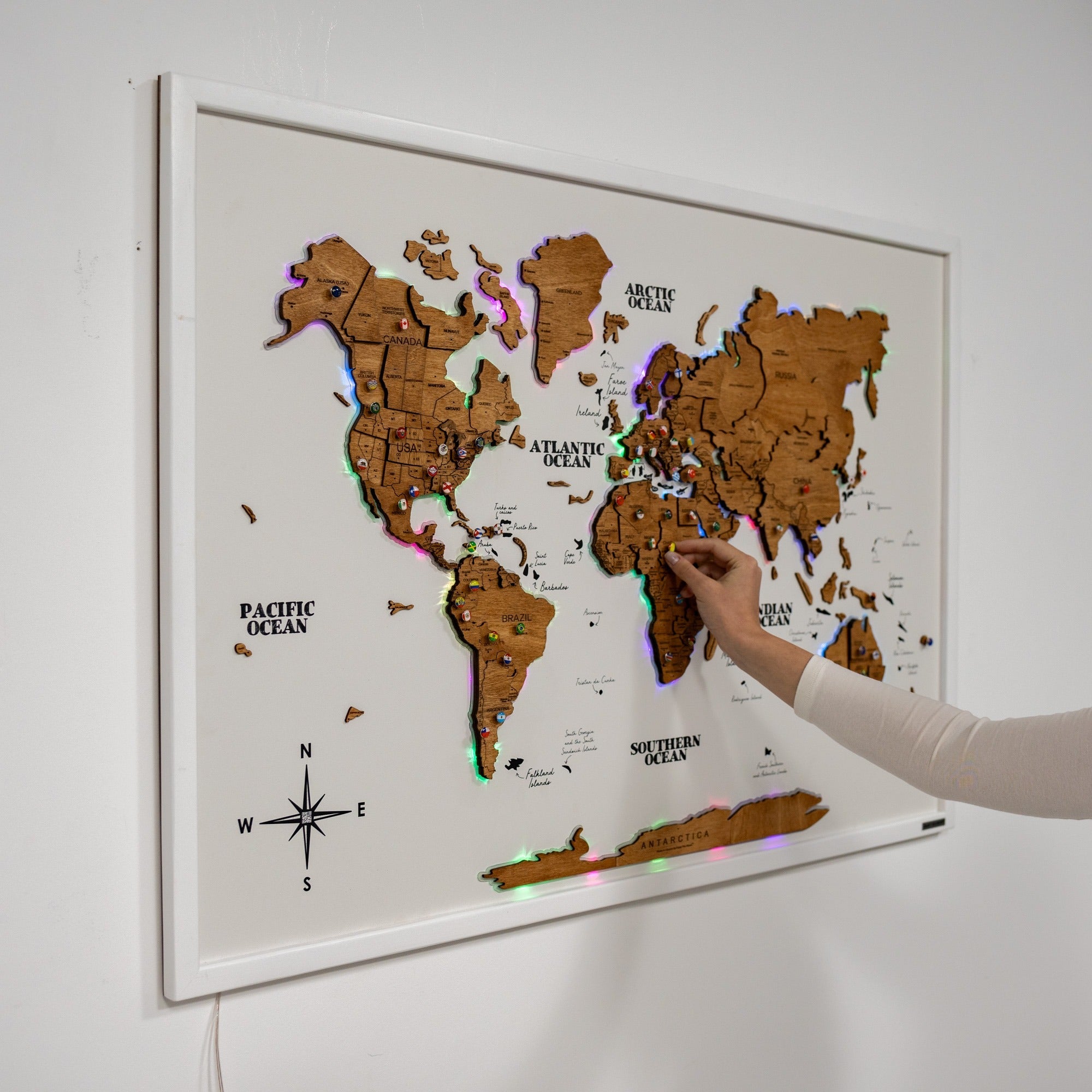 World map with LED lights on a white wall, hand touching the map