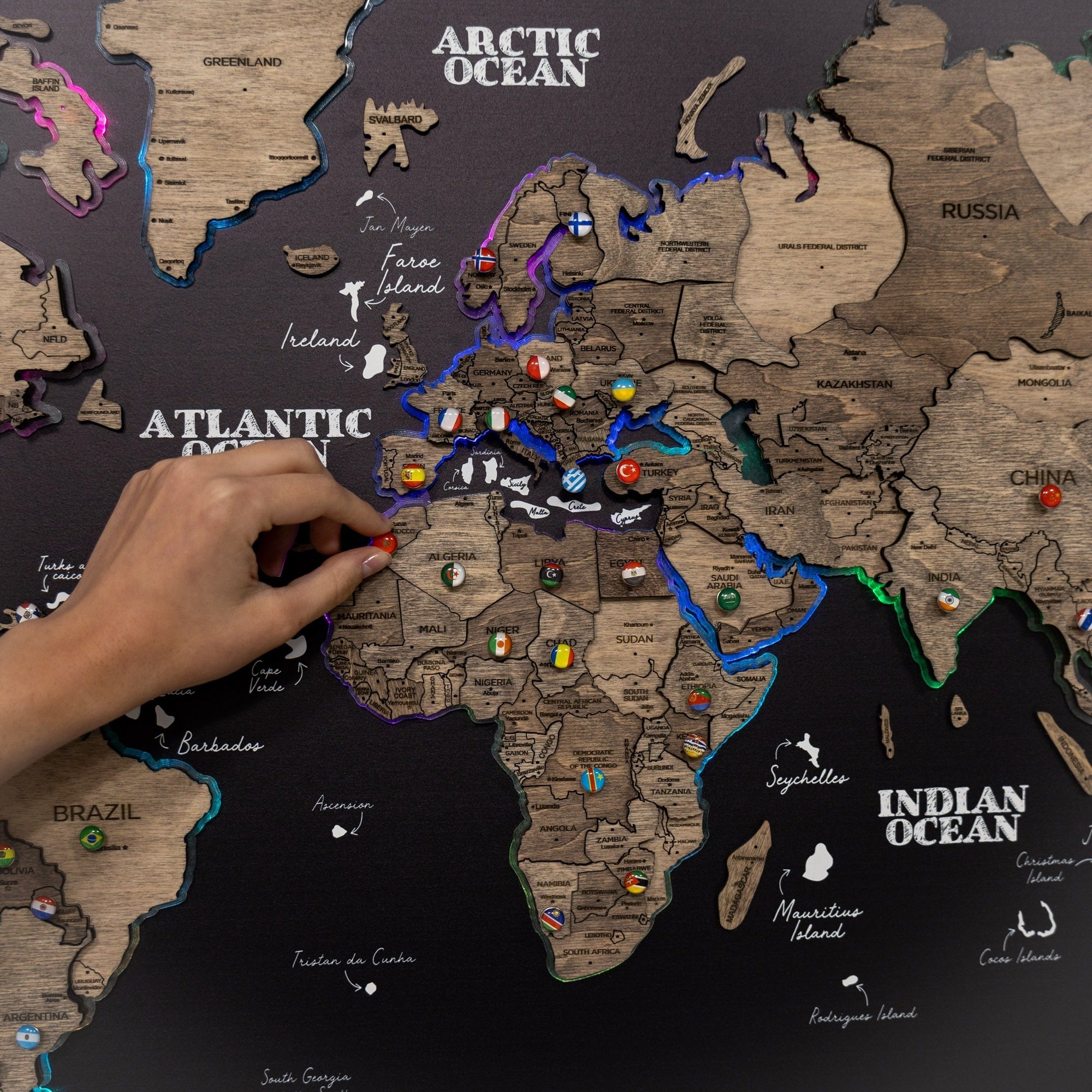 World map with wooden cutout countries and hand placing a red pin on a location.