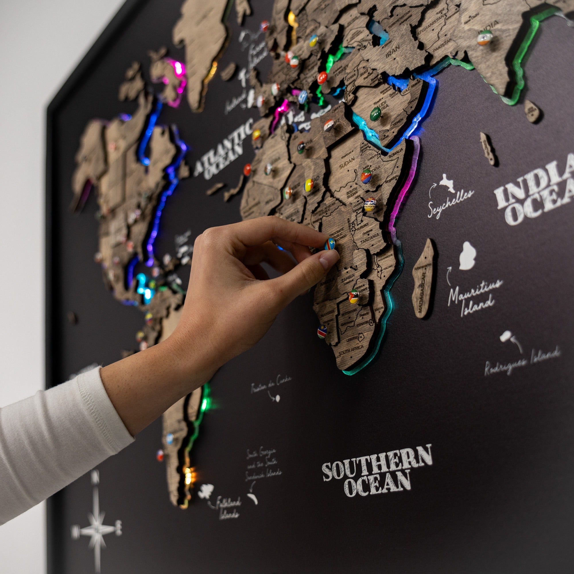 World map with colorful pins on a dark background, hand pointing to a location.
