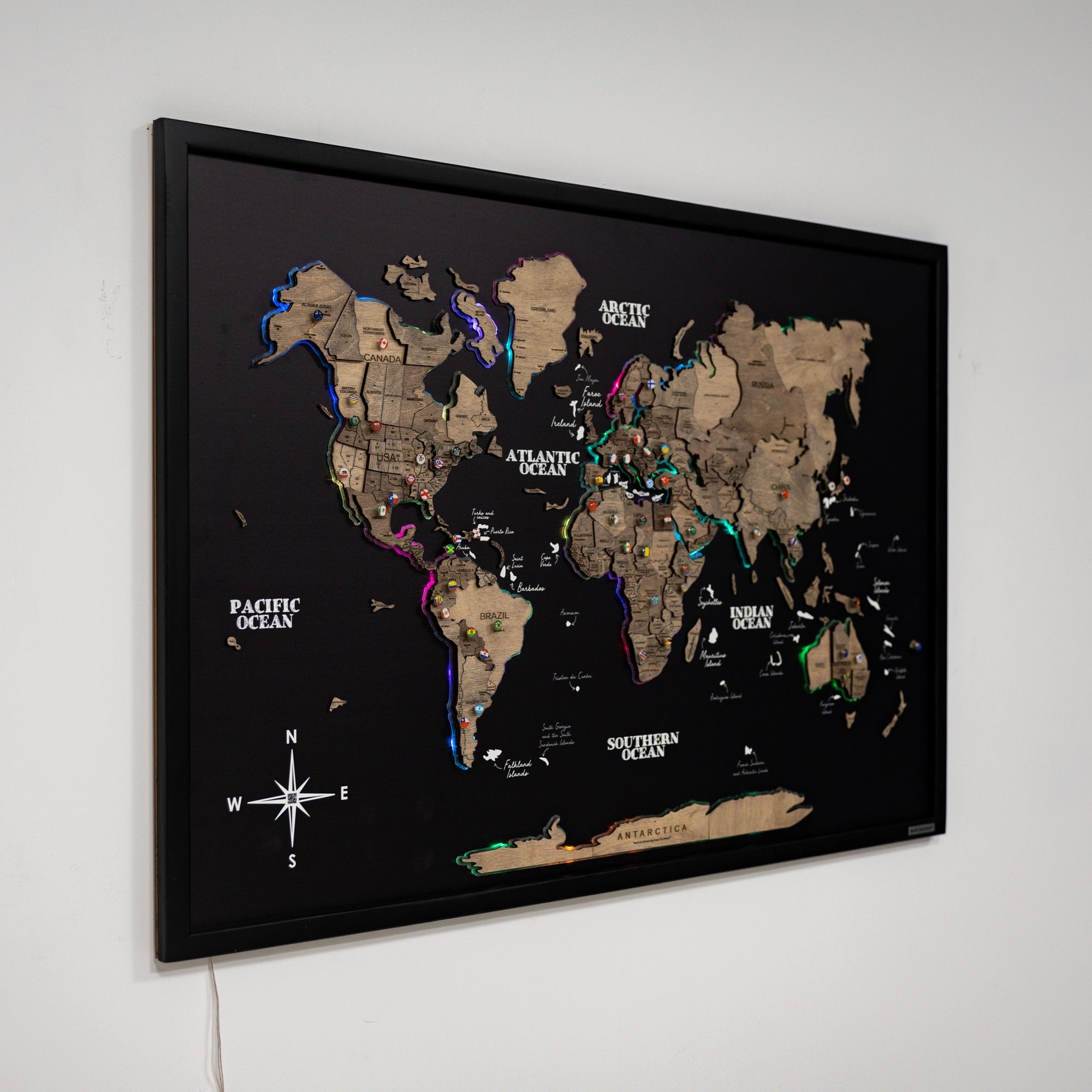 World map with push pins on a black background, framed and mounted on a wall.
