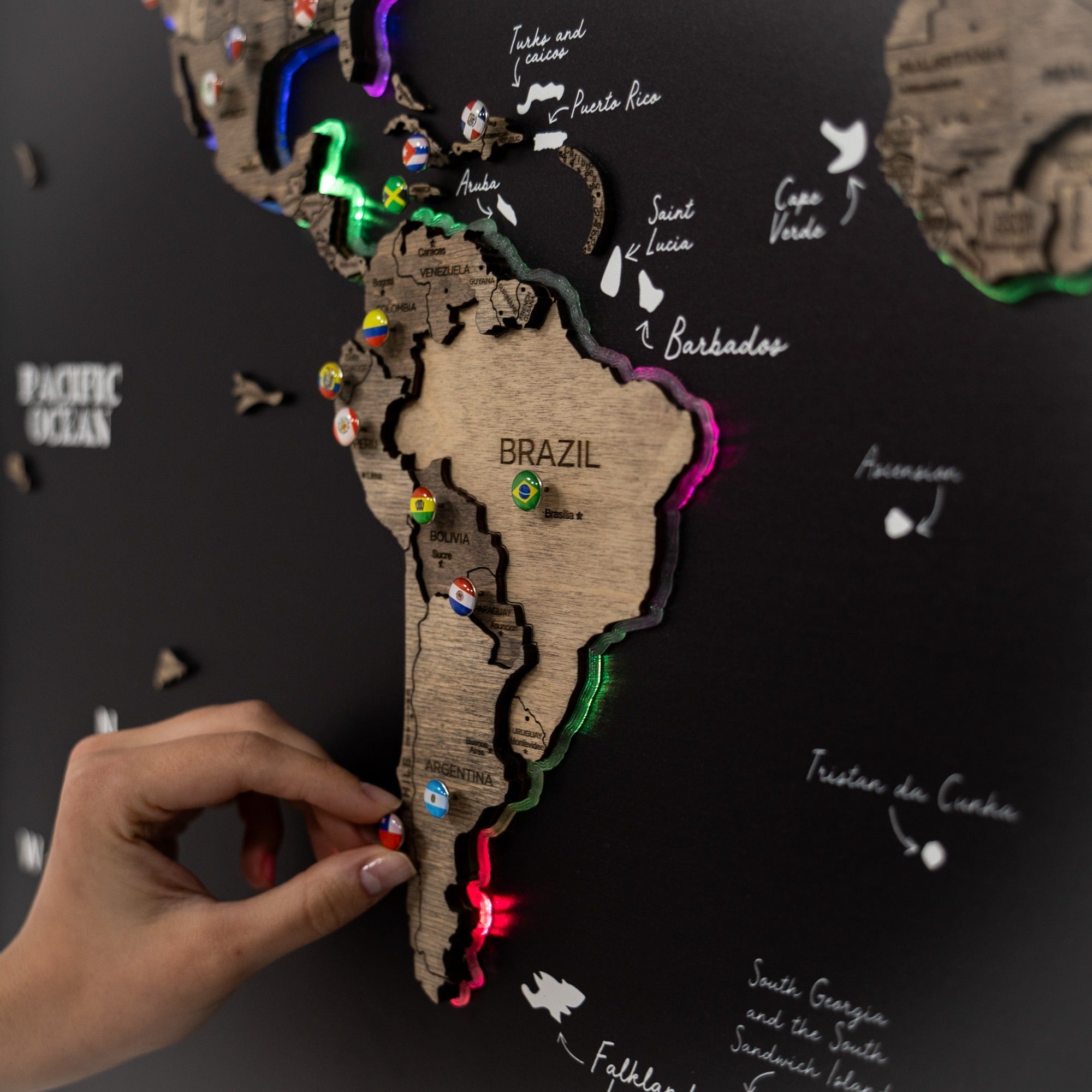 Wooden map of South America with colorful pins on a dark background